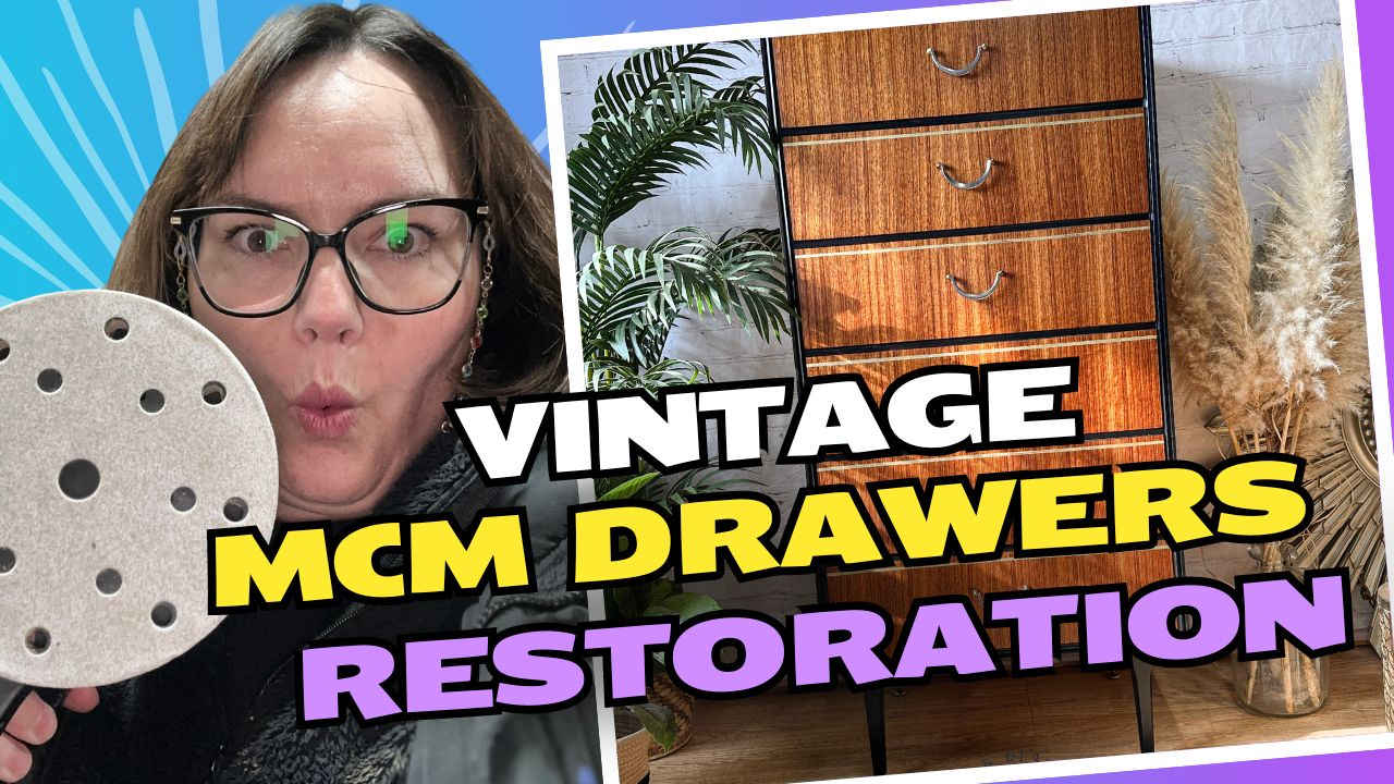 A person holding a sanding disc poses next to a restored mid-century modern chest of drawers. Bold text reads "VINTAGE MCM DRAWERS RESTORATION". The background includes plants and dried grasses. The overall setting suggests a restoration or DIY project.