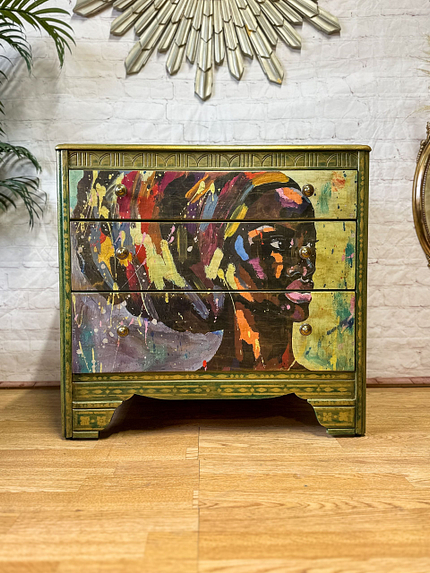 The Bohemian Green & Gold: Revamped Harris Lebus MCM Chest of Drawers boasts three drawers adorned with a vibrant, abstract painting of a person's head in profile. The artwork on the drawers features colorful brushstrokes in shades of red, purple, yellow, and blue. The dresser stands on a wooden floor with a white brick wall in the background.