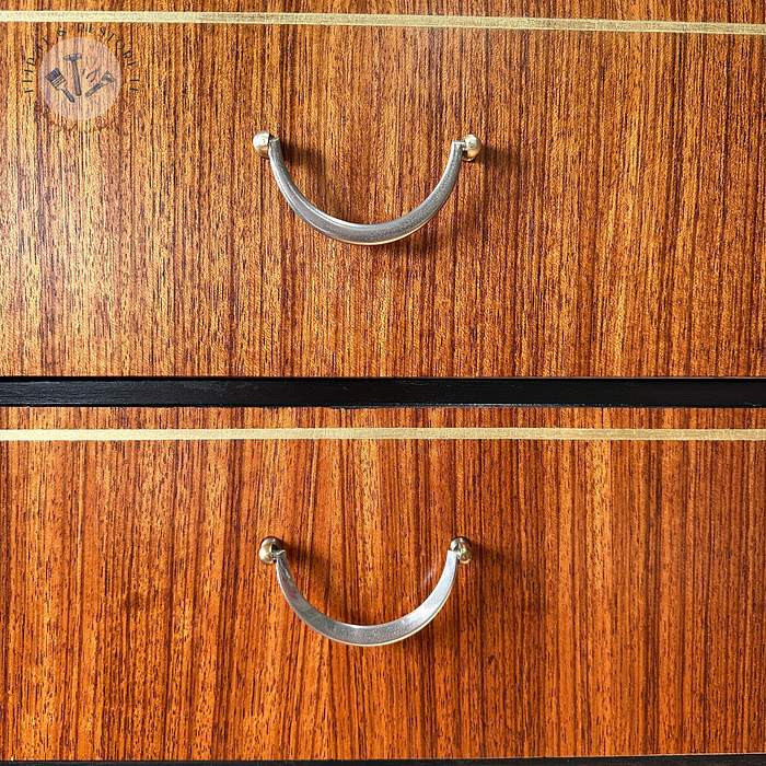 Close-up of two metallic, arch-shaped handles on the Exquisite Mid Century MCM Walnut Tallboy 6 Drawers Chest Of Drawers by Meredew, showcasing its rich brown wood grain. The handles are secured with small round mounts. In the top left corner, a faint circular logo with barely discernible markings can be seen.