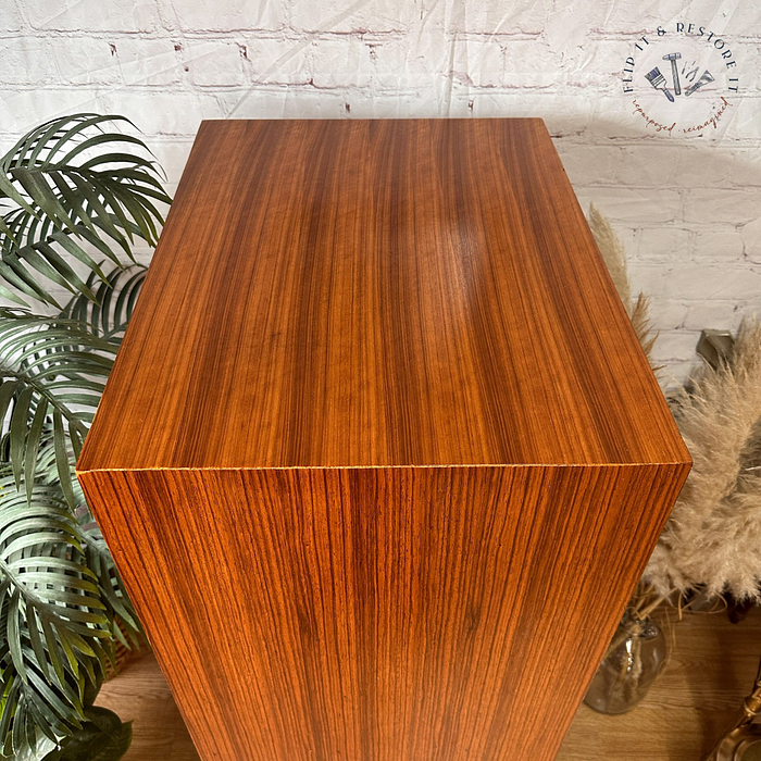 An Exquisite Mid Century MCM Walnut Tallboy 6 Drawers Chest Of Drawers by Meredew stands on a wooden floor. A potted plant with green leaves is placed beside it on the left. The background features a white brick wall and a circular logo with the text "Pick it, Restore it" in the top right corner.