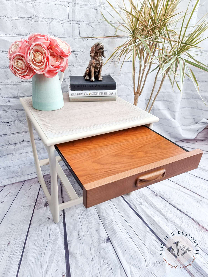 A Mid Century Beautility Drinks Cabinet, Vintage 1960's Walnut Cocktail Bar, featuring an open drawer. The top of the cabinet displays a vase with pink roses, two stacked books, and a small dog figurine. A plant with long, slender leaves is seen in the background. A circular logo with text is positioned in the bottom right corner.