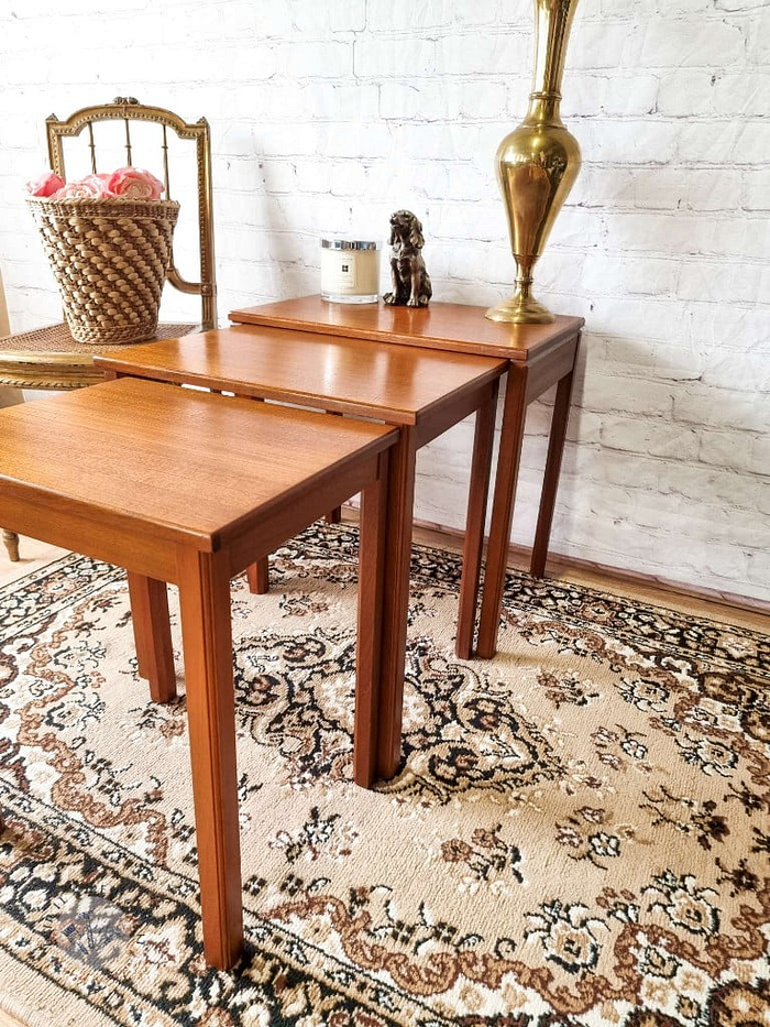 The Ercol Saville Ash Long Coffee Table with Smoked Glass Mid Century Vintage is placed on an ornate rug with brown and beige patterns. On the table, there is a tall, golden vase, a ceramic dog figurine, and a candle. In the background, there's a chair with a basket of pink flowers.