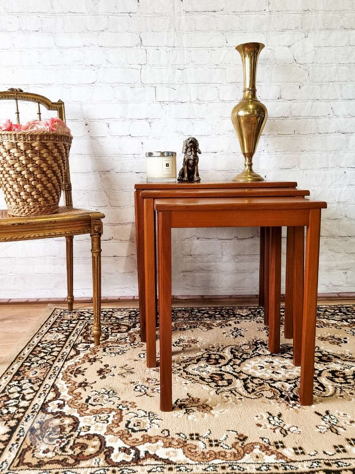 An Ercol Saville Ash Long Coffee Table with Smoked Glass Mid Century Vintage is arranged on a decorative rug with intricate patterns against a white brick wall. On the table, there are a tall brass vase, a small candle, and a ceramic figurine. A woven basket on a chair is partially visible on the left.