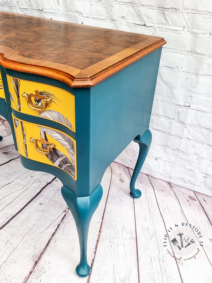 A Queen Anne Painted Burr Walnut Dressing Table/Vanity/Desk/Sideboard featuring teal-painted cabriole legs and sides, with two drawers that have yellow fronts adorned with feather designs. The tabletop showcases a rich wood grain finish. A small logo in the bottom right corner reads "Flip It & Restore It," against a white brick background.